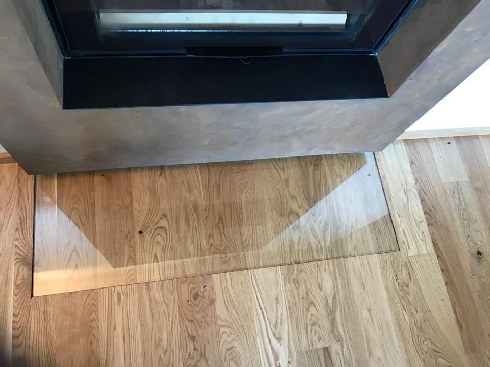 Un socle en verre transparent repose sur un parquet en chêne clair, devant un insert de cheminée moderne aux tons sombres.