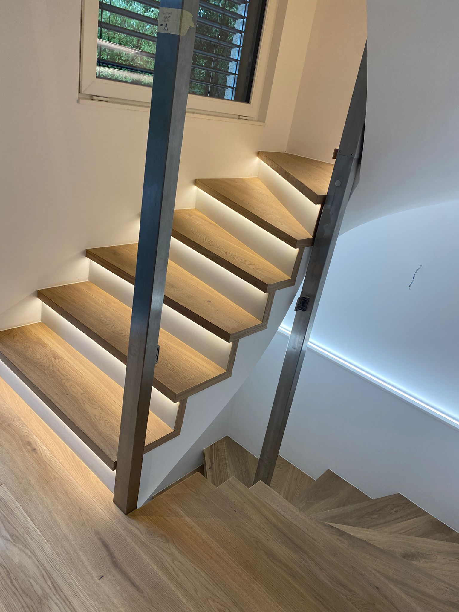 Escalier moderne en bois avec éclairage LED sous les marches et rampe métallique élégante, dans un intérieur contemporain.