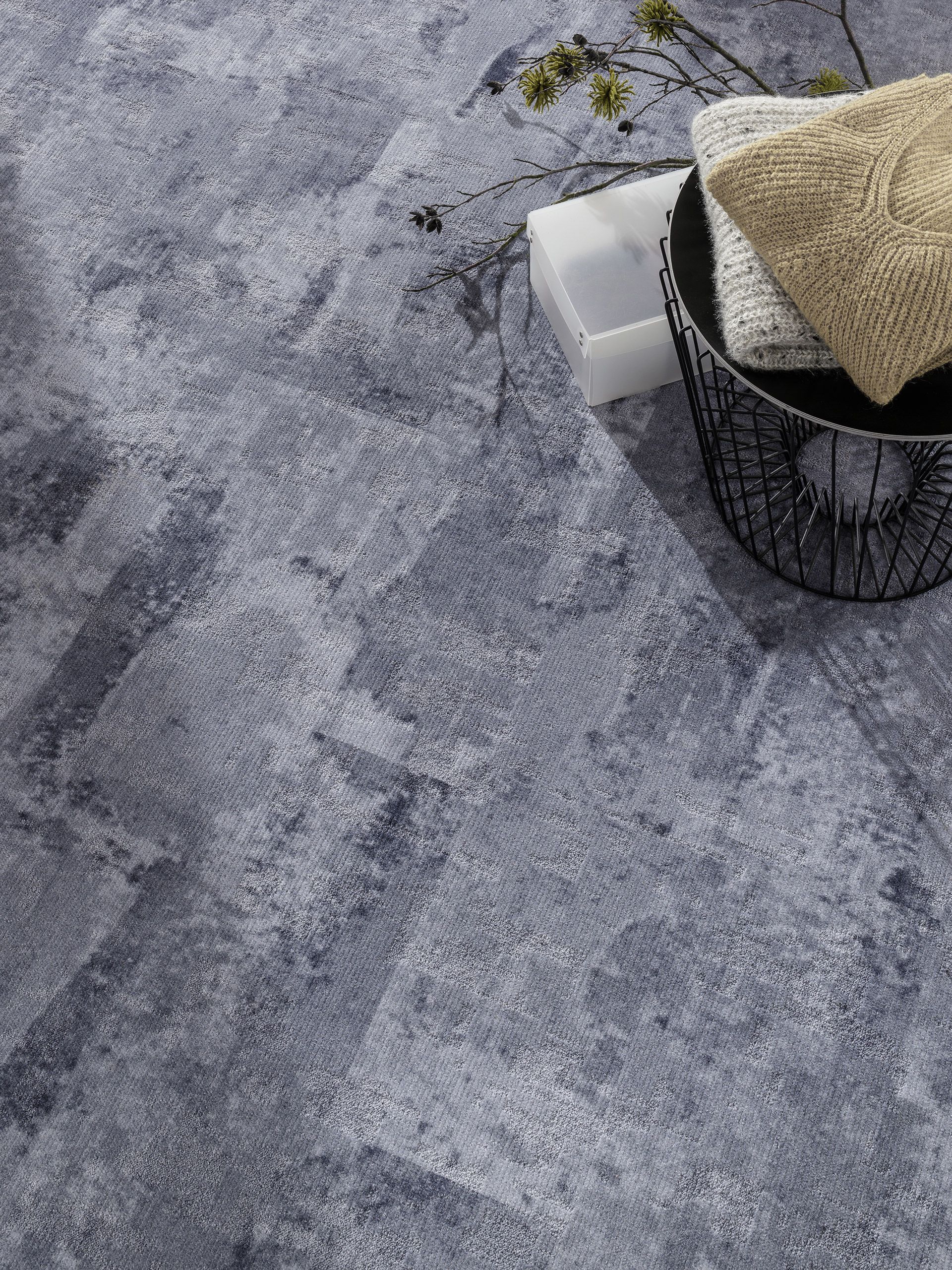 Une surface texturée, effet pierre bleu foncé, avec un panier décoratif en fil de fer contenant des textiles beiges et blancs pliés.