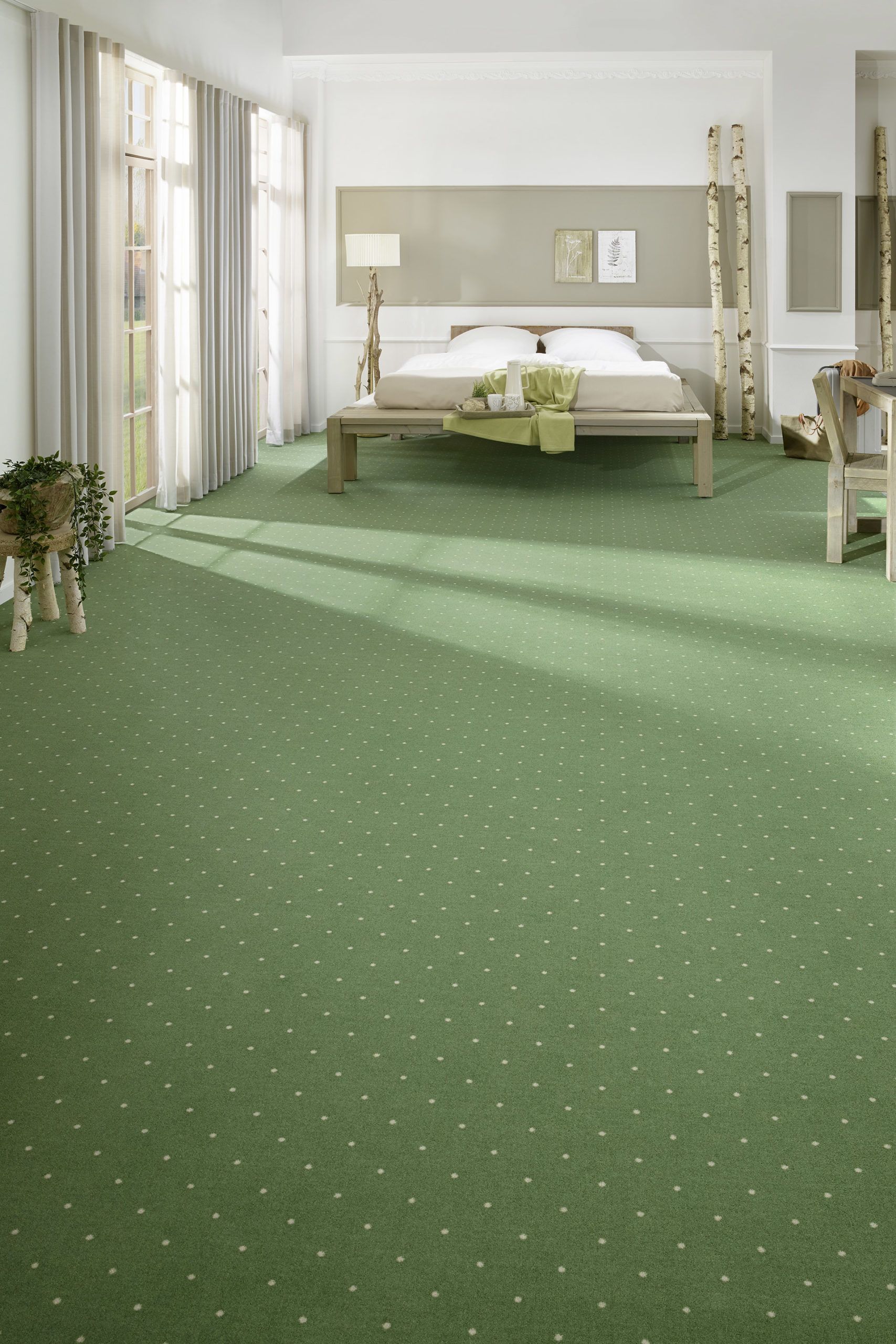 Une chambre avec une moquette vert sauge à pois blancs, un lit avec des draps blancs et de hautes fenêtres avec des rideaux transparents.