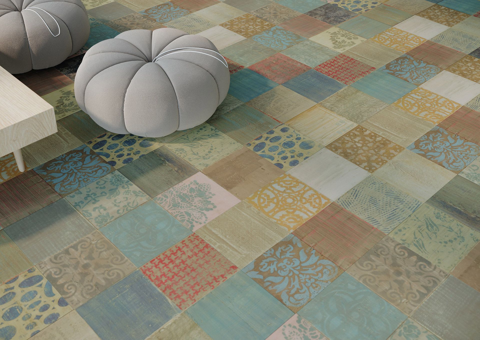 Un tapis patchwork multicolore composé de carreaux carrés aux motifs délavés dans les tons bleus, beiges et rouille, est disposé à côté de poufs.