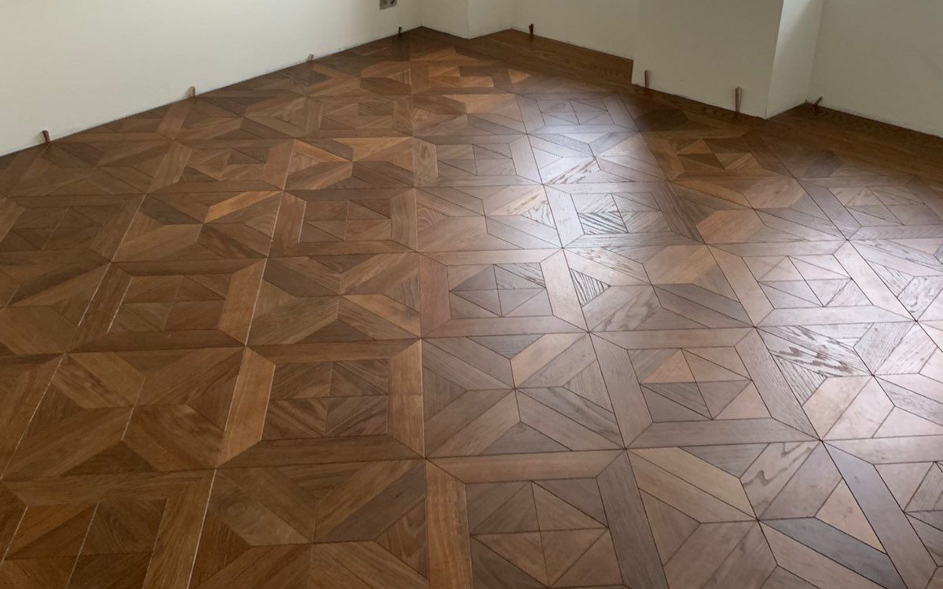 Une pièce ornée d'un parquet en bois de style Versailles aux motifs géométriques complexes, dans des tons bruns chauds.