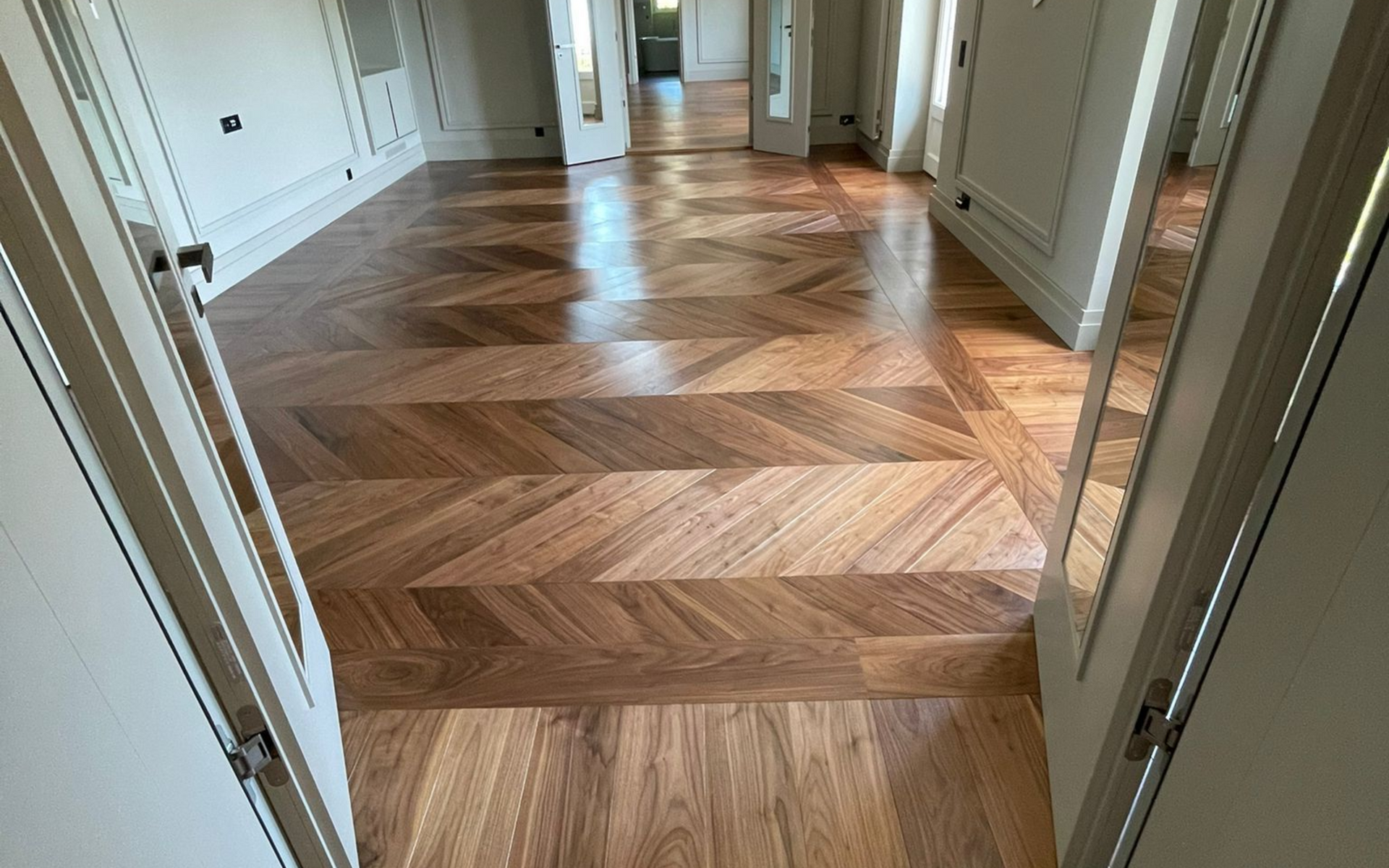 Vue, à travers une porte, d'une pièce au parquet en bois clair poli, posé en chevrons.