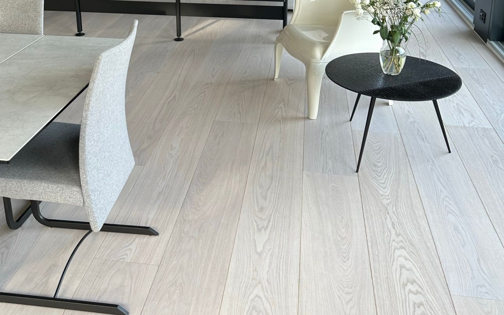 Un salon moderne avec un parquet clair, une chaise de salle à manger grise texturée, un fauteuil blanc et une petite table noire.