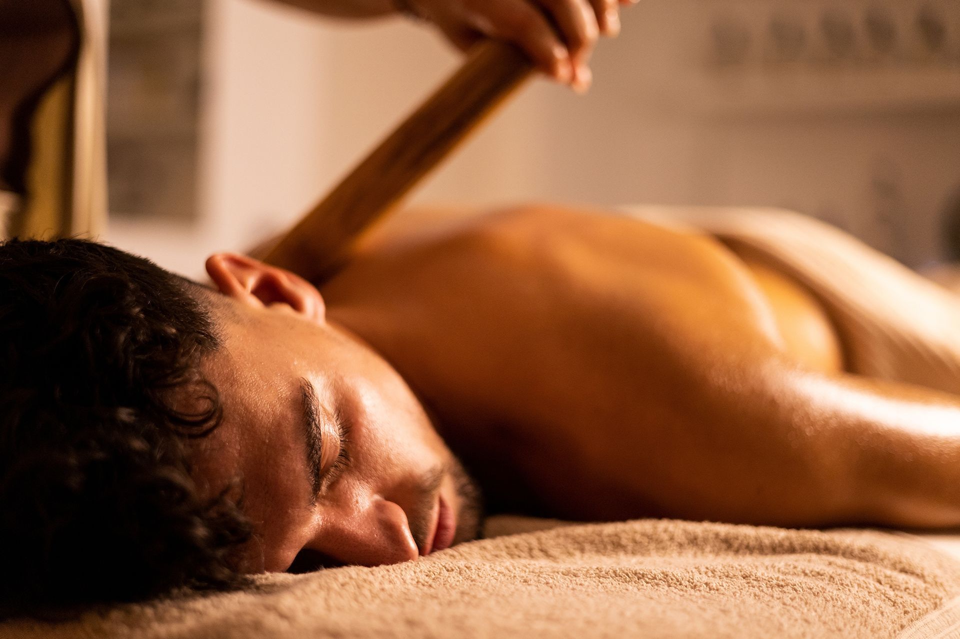 A man is laying on a bed getting a massage with a wooden stick.