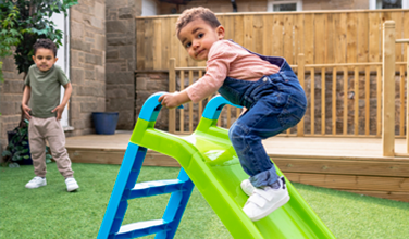 Two young boys are playing on a slide in a backyard.