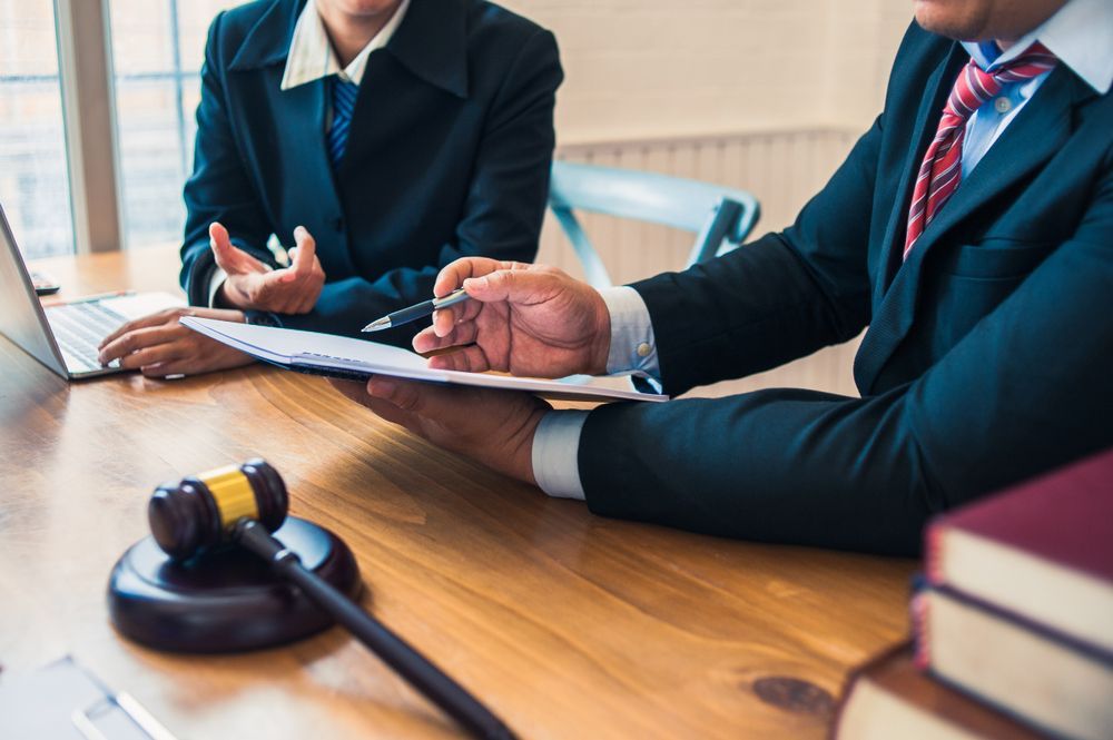 A Man And A Woman Are Sitting At A Table With A Laptop And A Gavel — Spencer Lawyers In Gosford, NSW