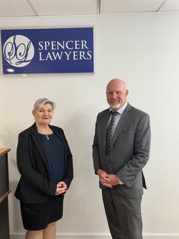 A Man And Two Women Are Posing For A Picture In Front Of A Sign For Spencer Lawyers — Spencer Lawyers In Gosford, NSW