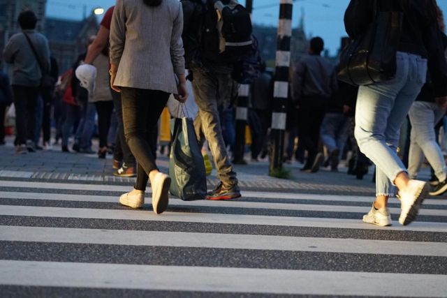 People walking across a zebra crosswalk in an urban setting at dusk.