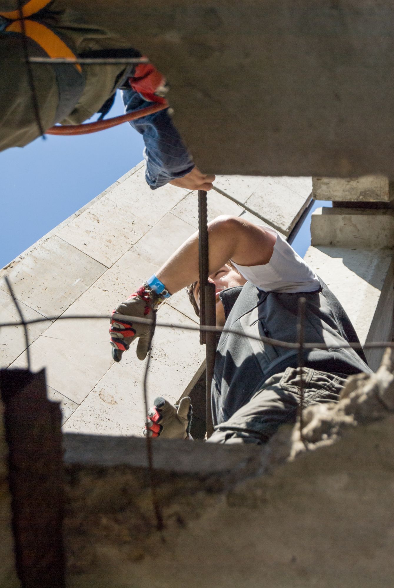 Man working with metal rods on a building, wearing gloves and safety harness.