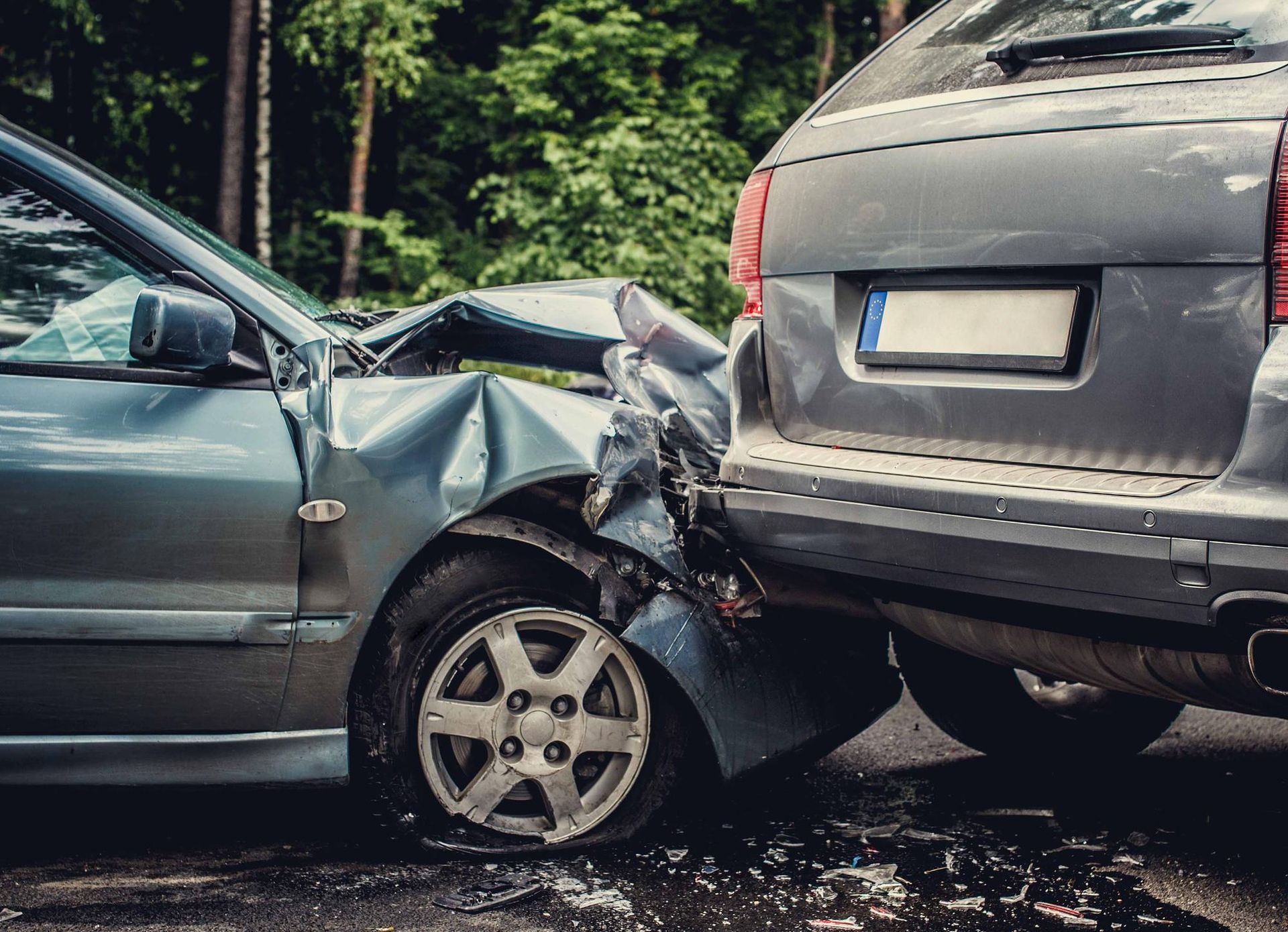Cars in a collision: a gray sedan's front is crushed into the rear of a gray SUV on a road.