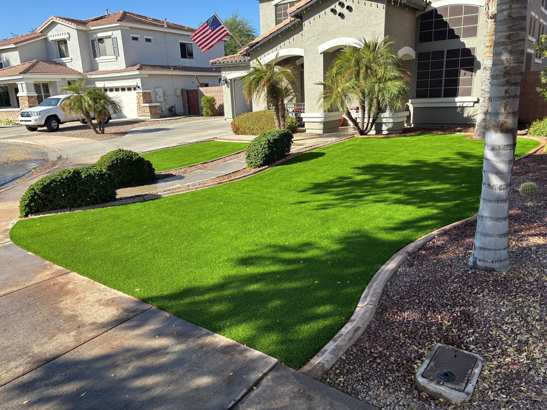 A front yard with vibrant green artificial turf. A house with an American flag in the background.