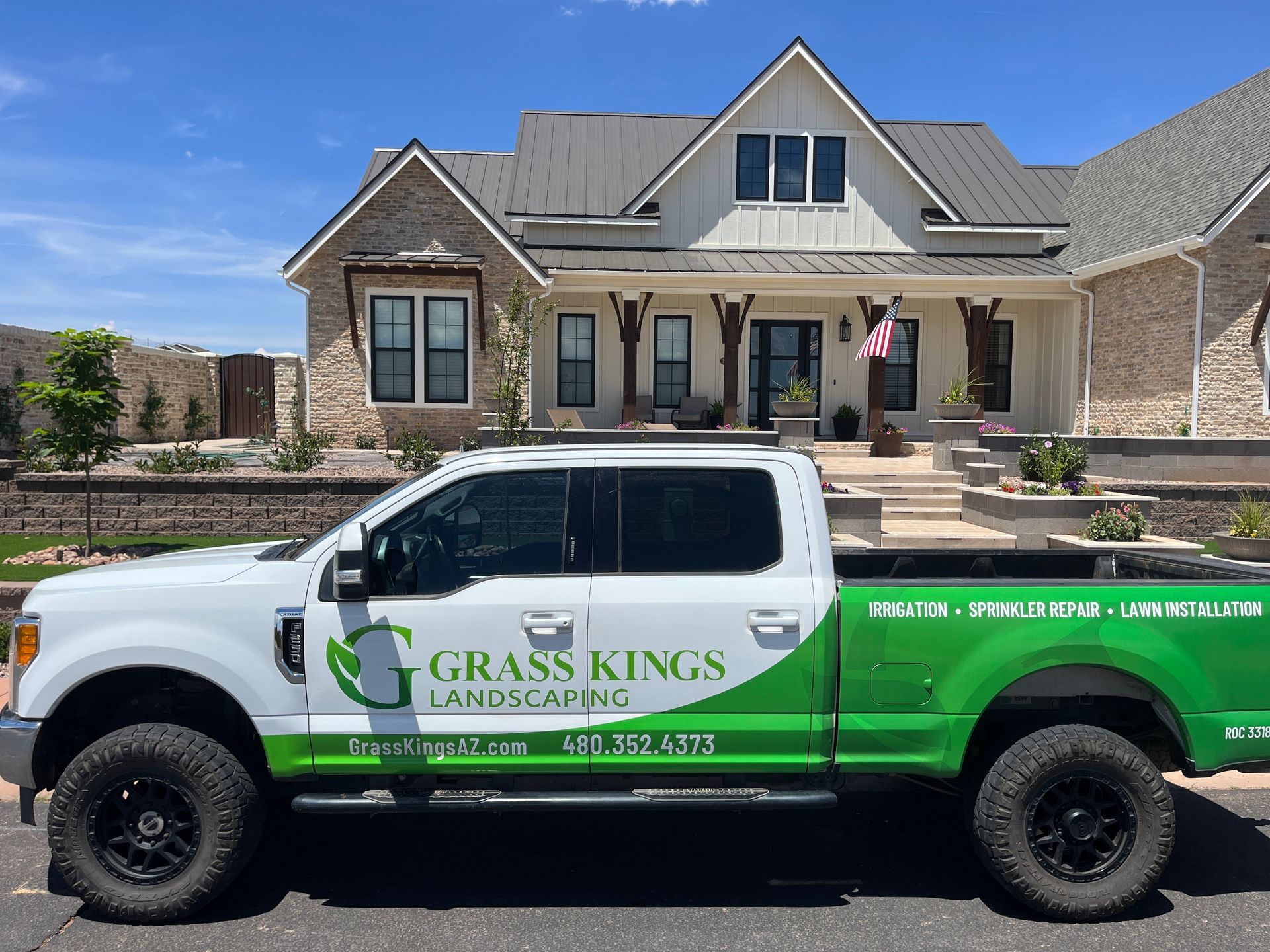 A white and green Grass Kings Landscaping truck parked in front of a large, modern house. The truck has large black tires.