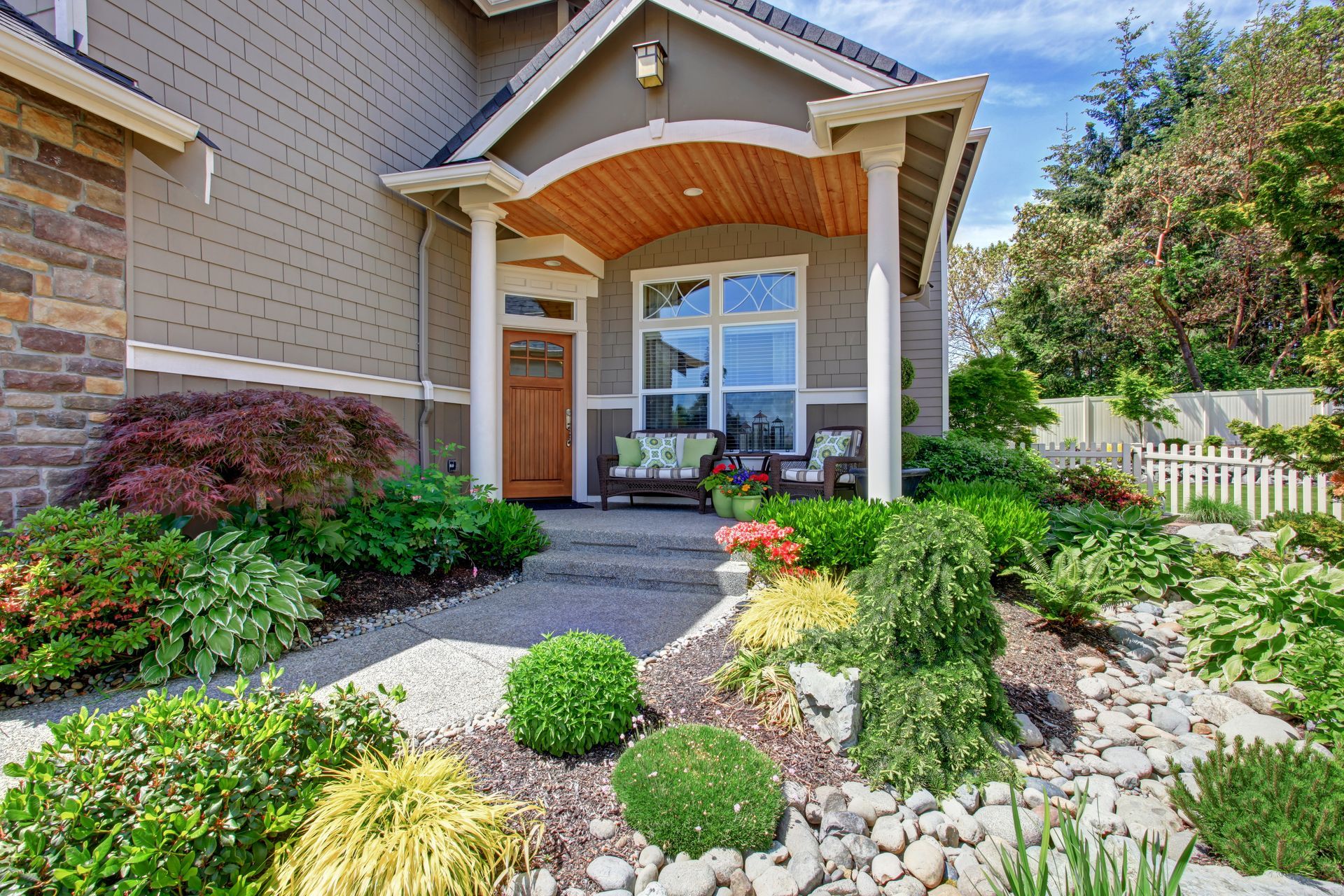 A house with a large porch and a lush green garden in front of it.