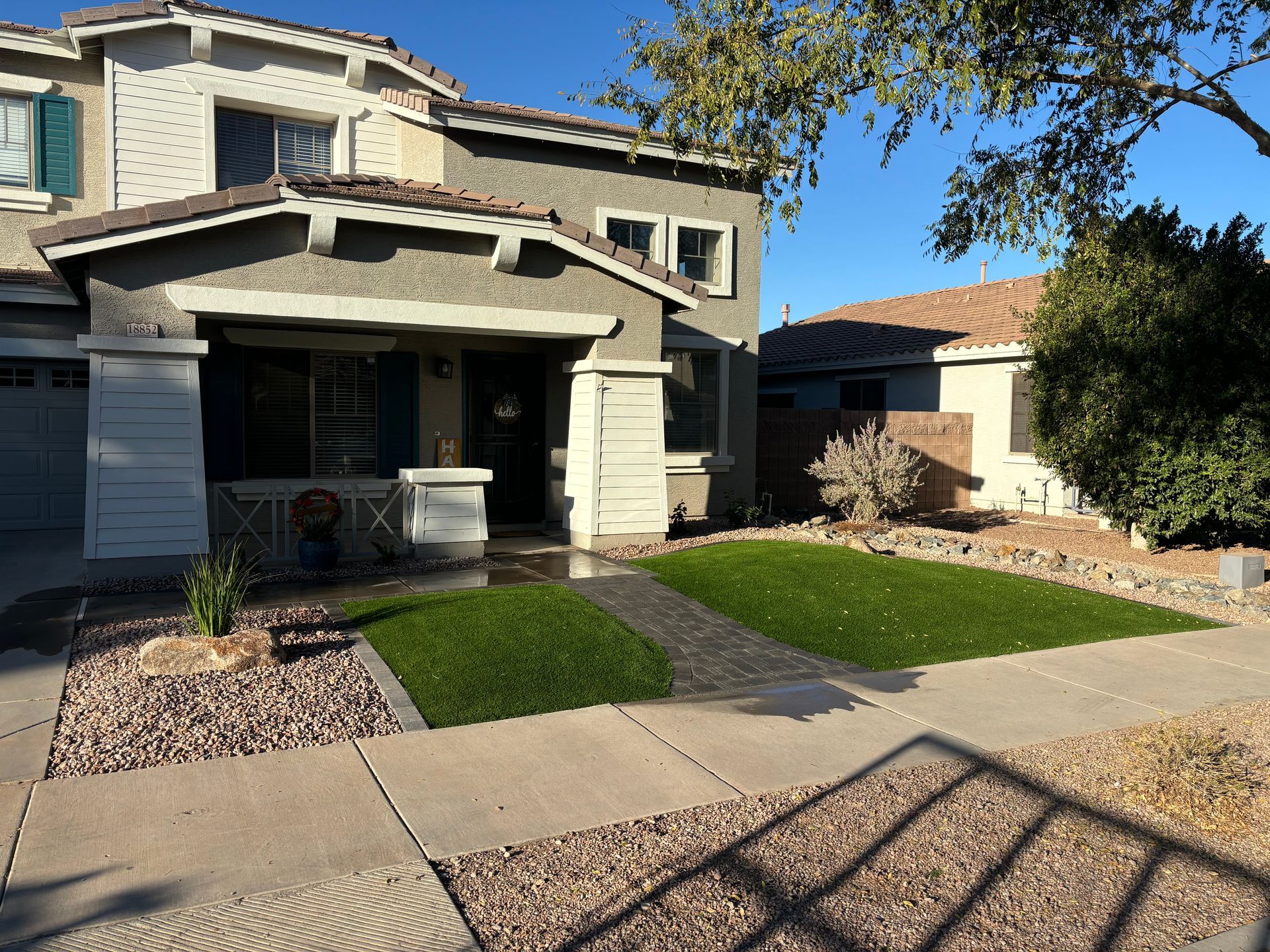 Two-story house with green lawn and gravel landscaping in front. Sunny day with blue sky.