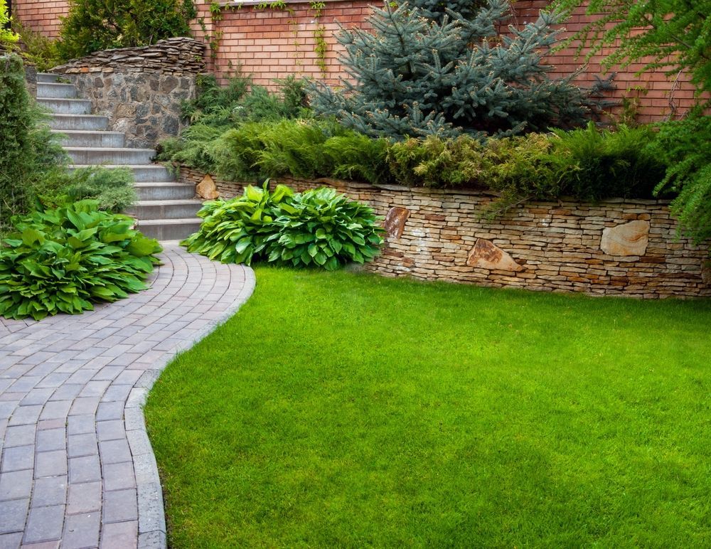 A lush green lawn with a curved stone path leading to steps, surrounded by landscaping and retaining walls.