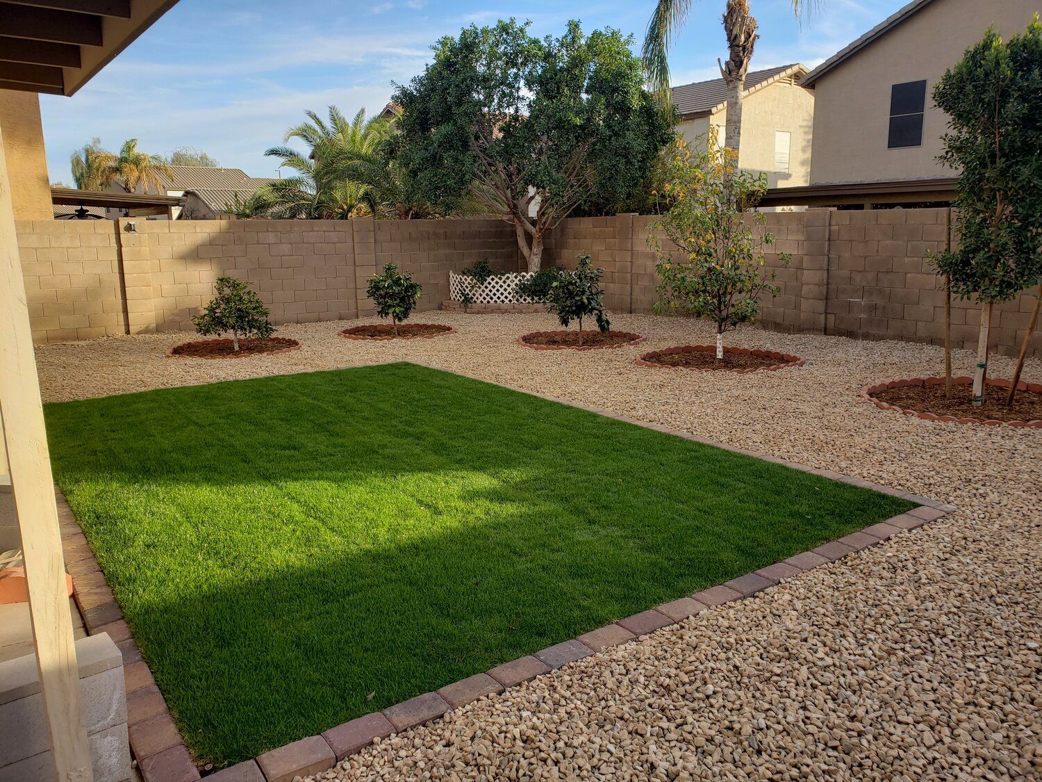 A backyard with a lush green lawn surrounded by gravel and trees.