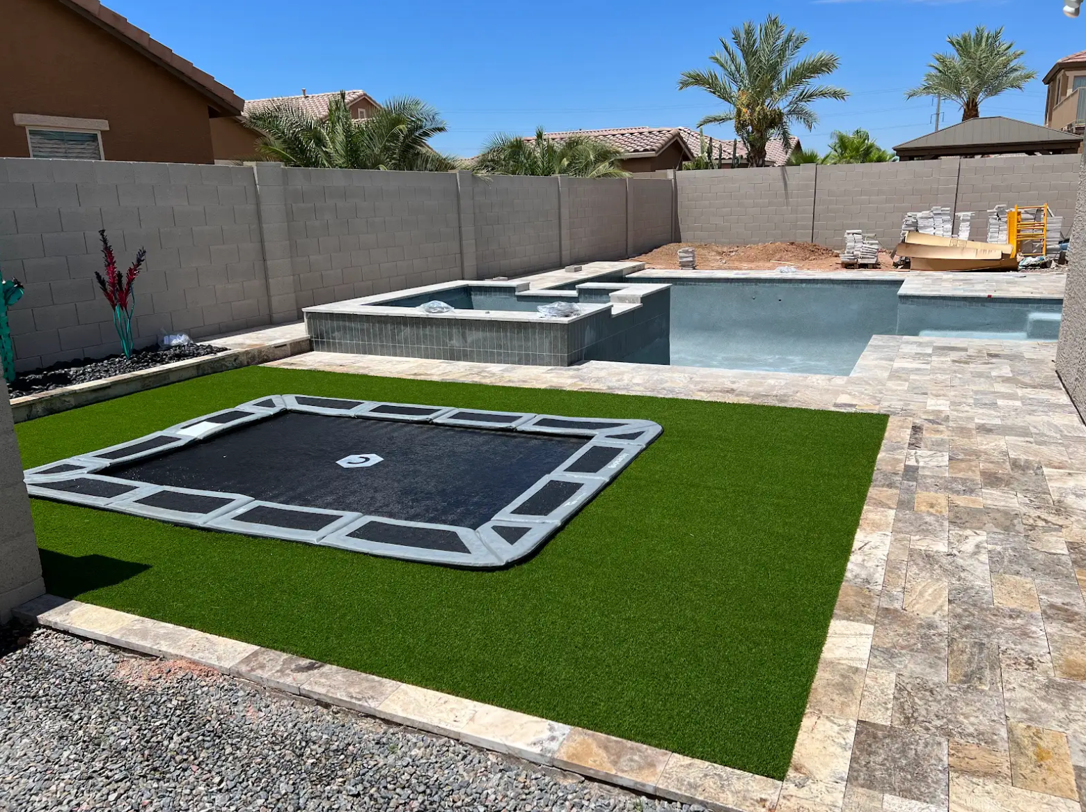 A trampoline is sitting on top of a lush green lawn next to a pool.