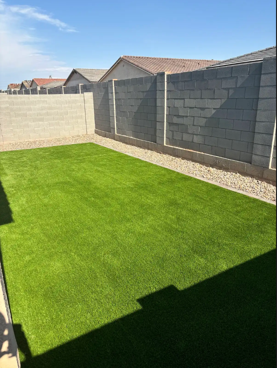 A backyard with a lush green lawn and a brick wall.