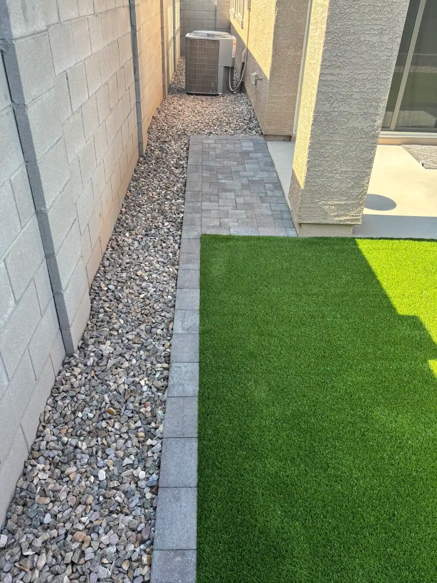 There is a walkway between a brick wall and a grassy area.