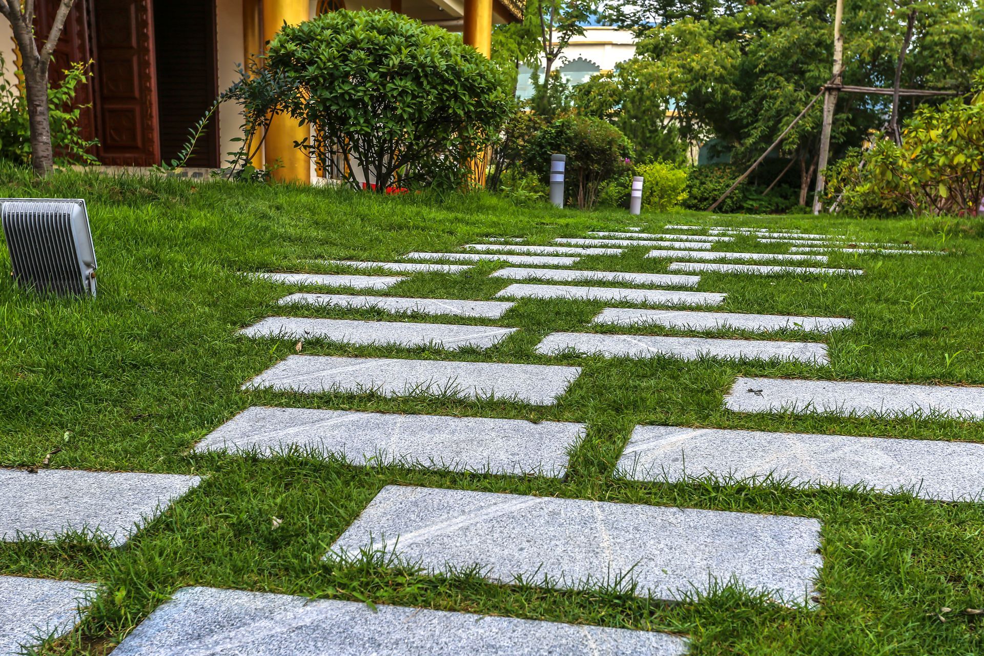 Stone path through green grass, leading toward a building and trees.