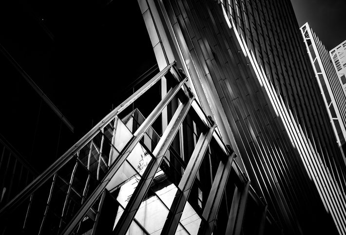 A black and white low-angle shot of a skyscraper's geometric steel framework and glass panels against a dark sky.