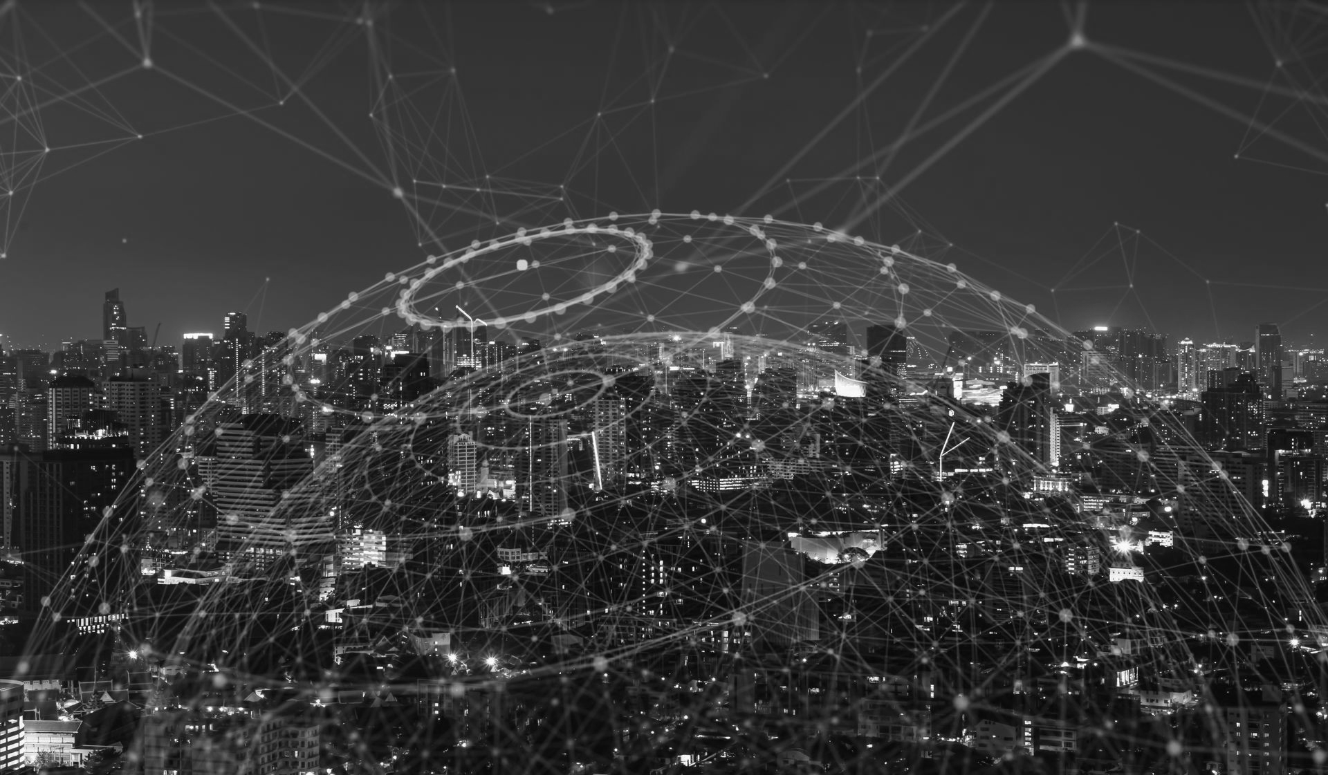 A grayscale cityscape at night overlaid with a glowing, digital network of intersecting lines and spheres.