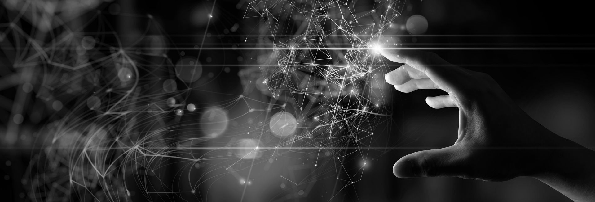 A black-and-white close-up of a hand reaching out to touch a glowing, abstract digital network of light particles.