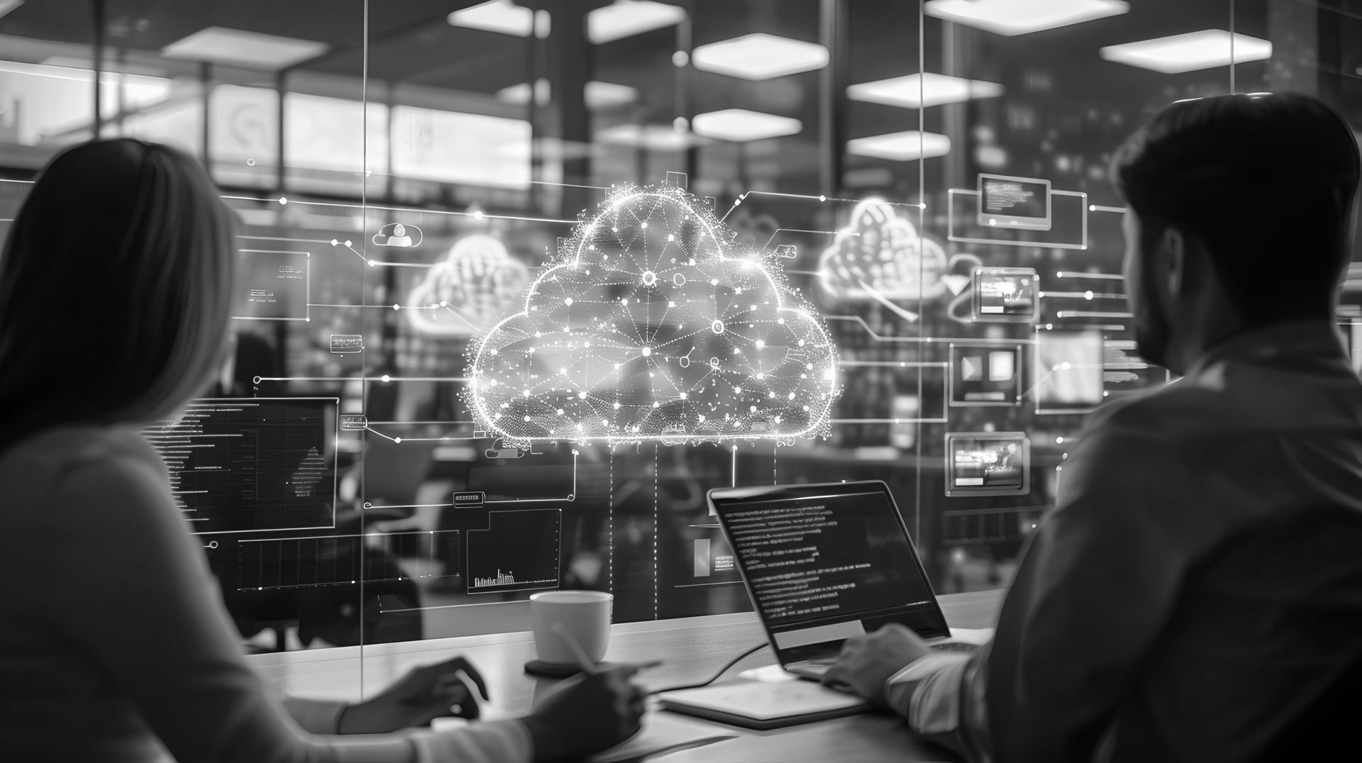 Two people working at a desk, looking at digital, glowing cloud computing graphics floating on a glass screen.