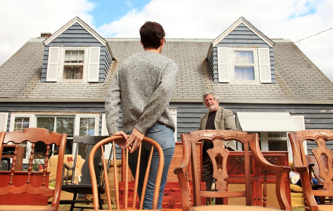 A woman is standing in front of a house surrounded by chairs.