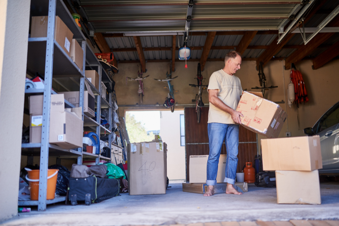 A man is standing in a garage holding a box.