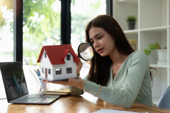 A woman is looking at a model house through a magnifying glass.