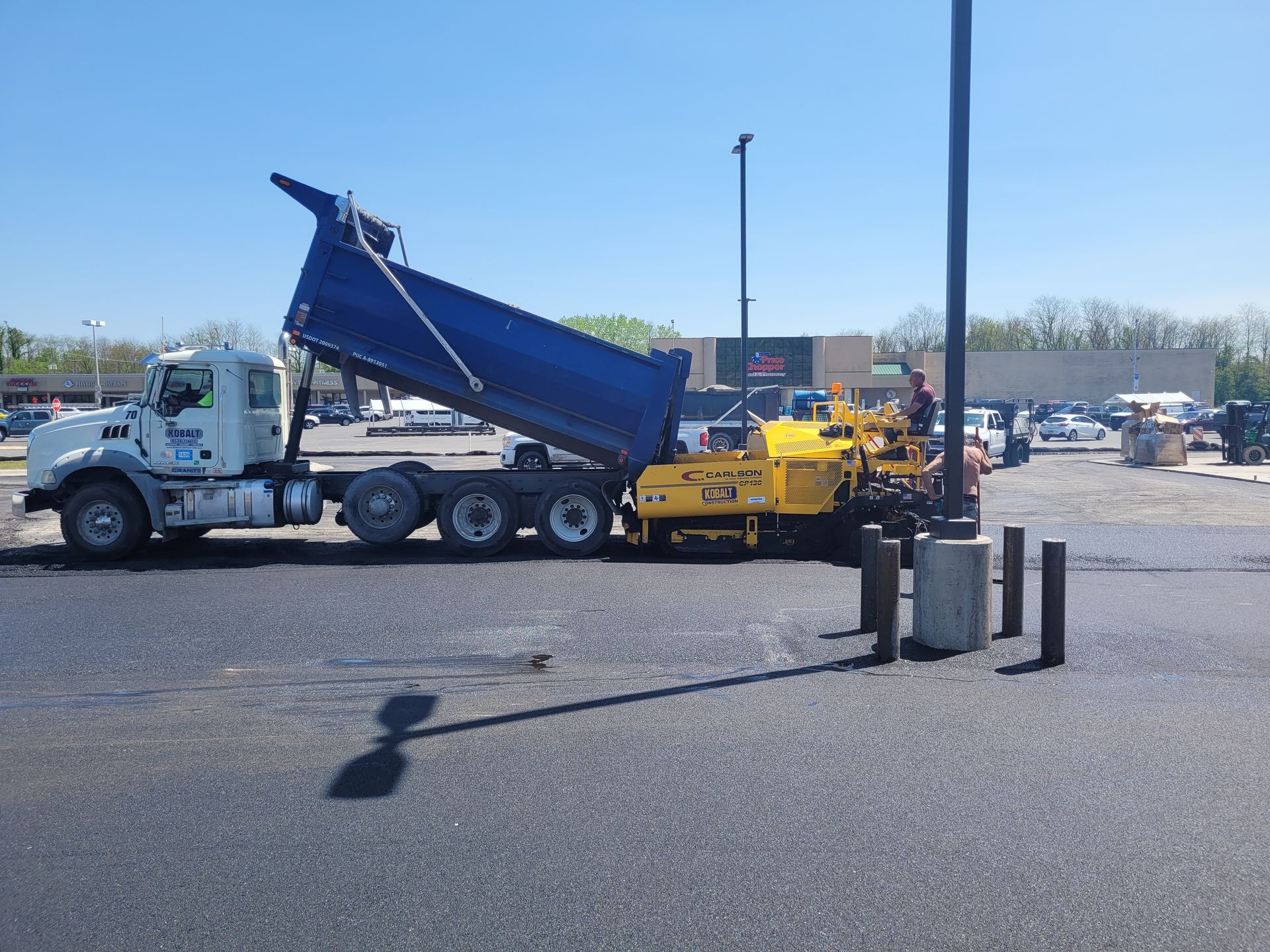 A dump truck is being loaded with asphalt in a parking lot.