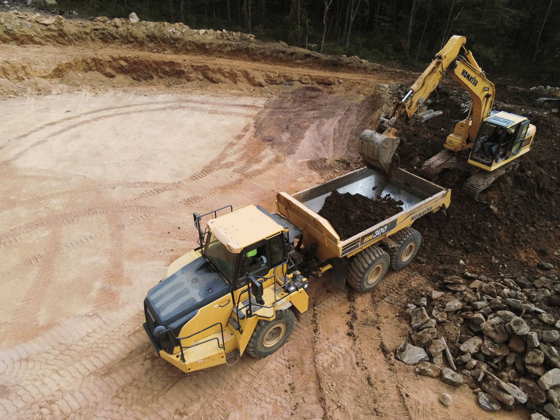 An aerial view of a dump truck and an excavator on a construction site.