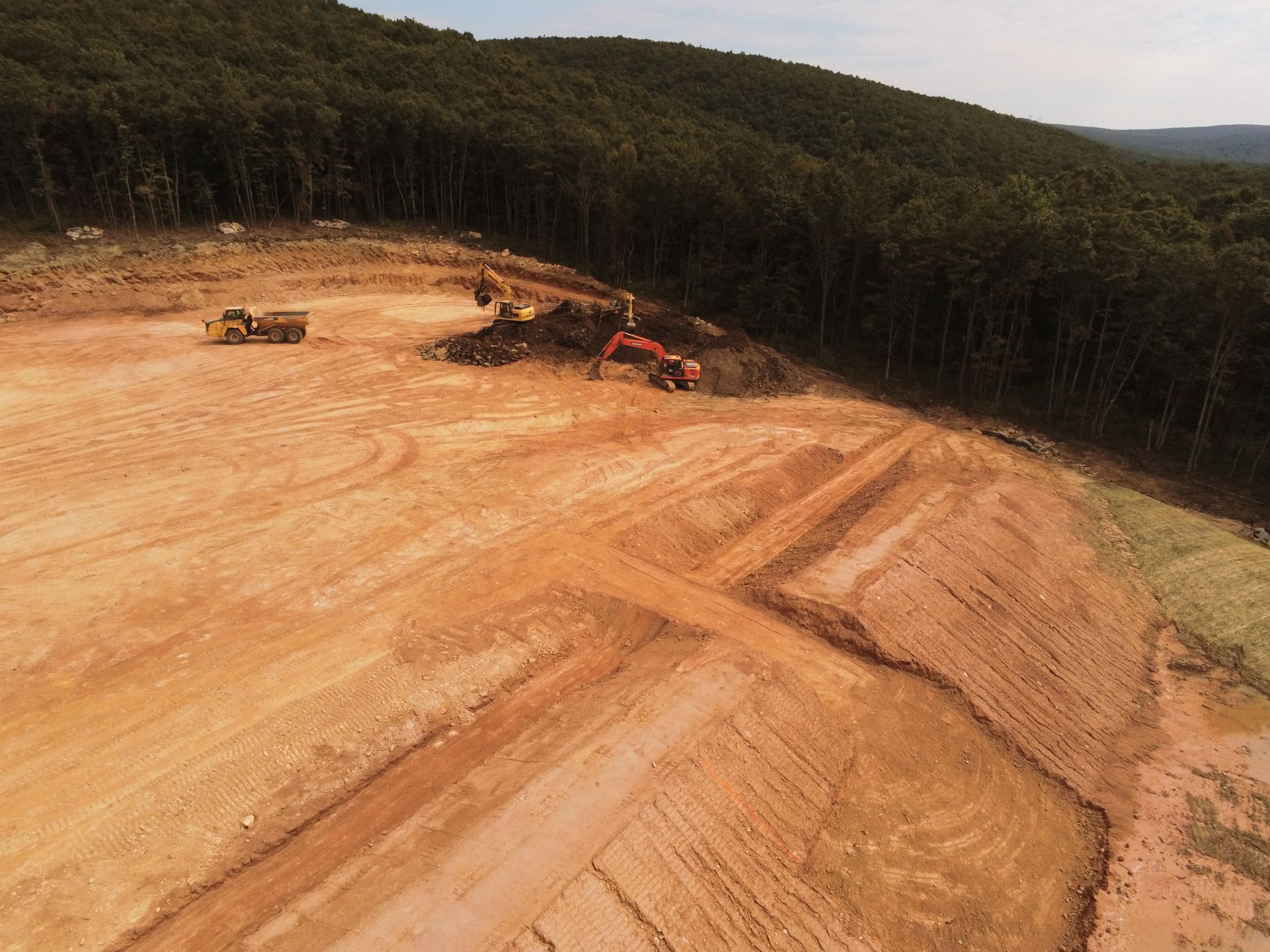 An aerial view of a construction site with a lot of dirt and trees in the background.