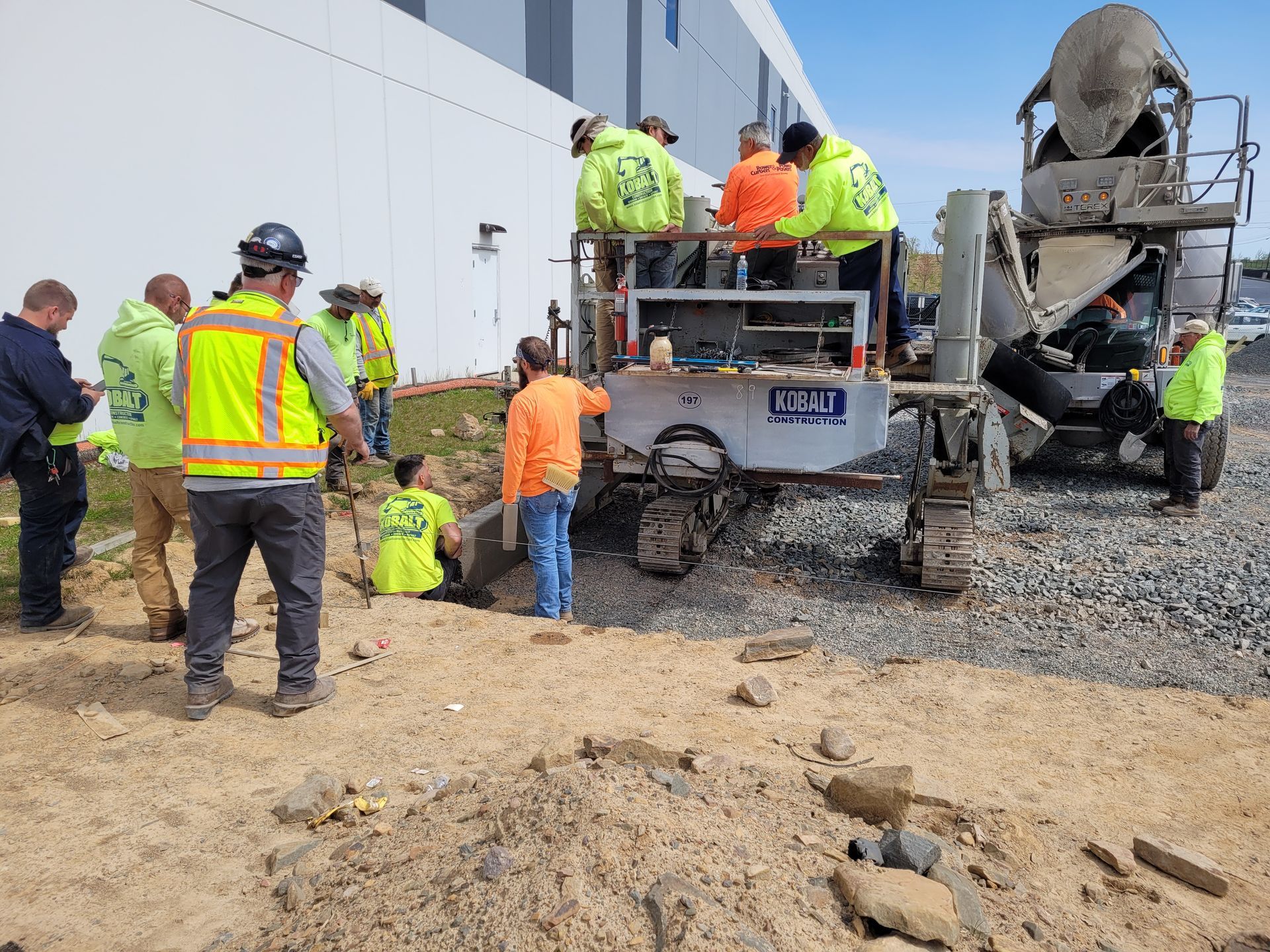 A group of construction workers are standing around a concrete mixer.