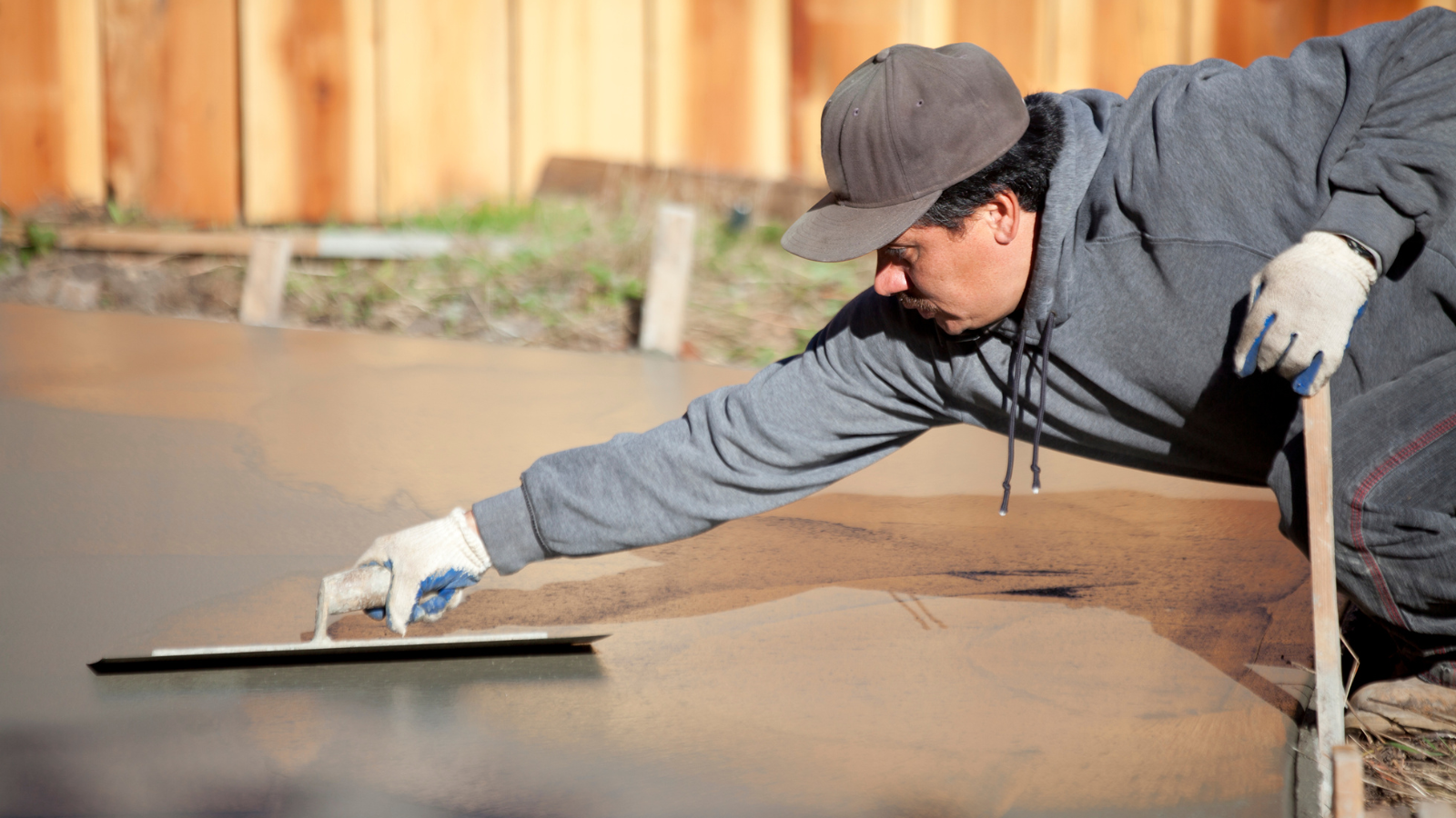 A man is laying concrete on a sidewalk with a trowel.