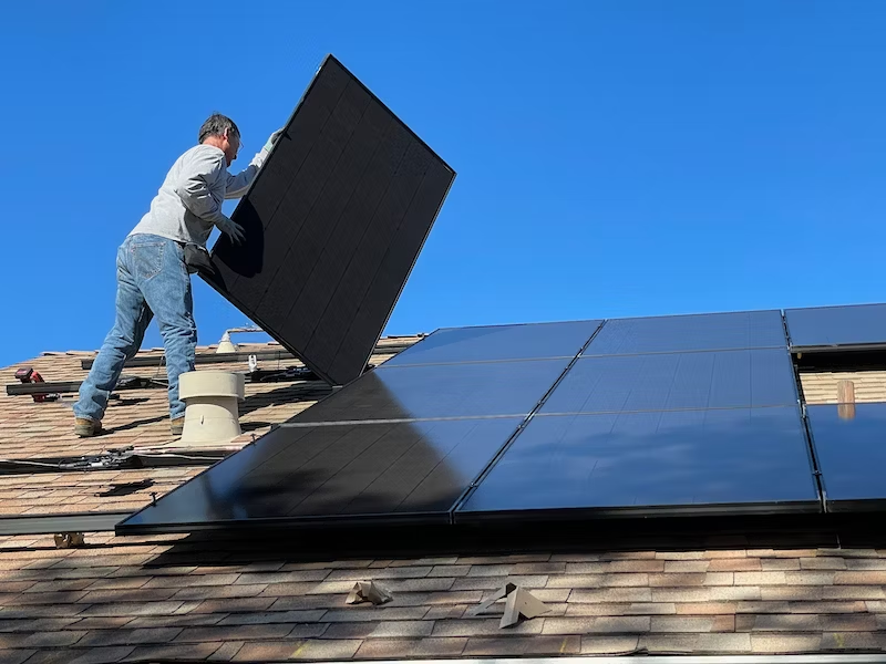 A man is installing solar panels on the roof of a house.