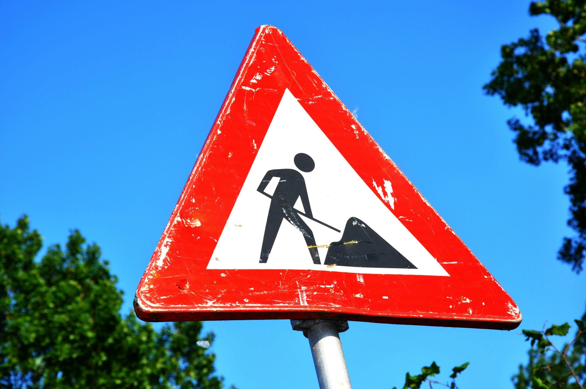 A construction zone sign surrounded by a blue sky and trees.