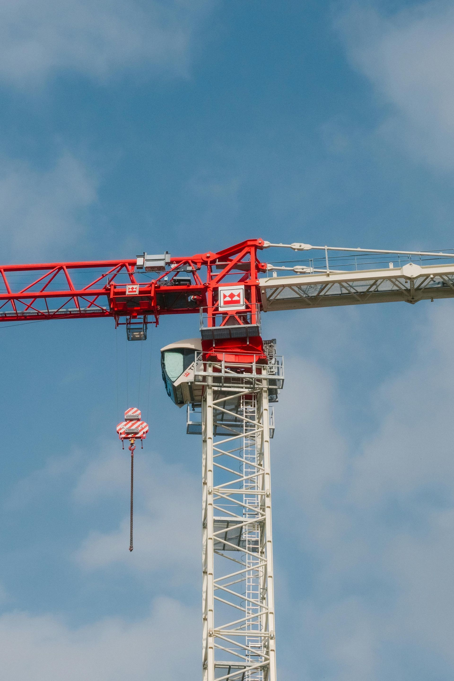 A red and white construction crane is against a blue sky with clouds.