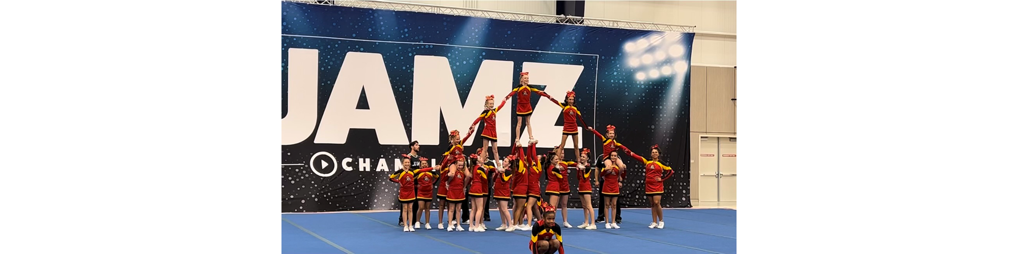 Dancers in red outfits performing on a stage in front of a large JAMZ banner.