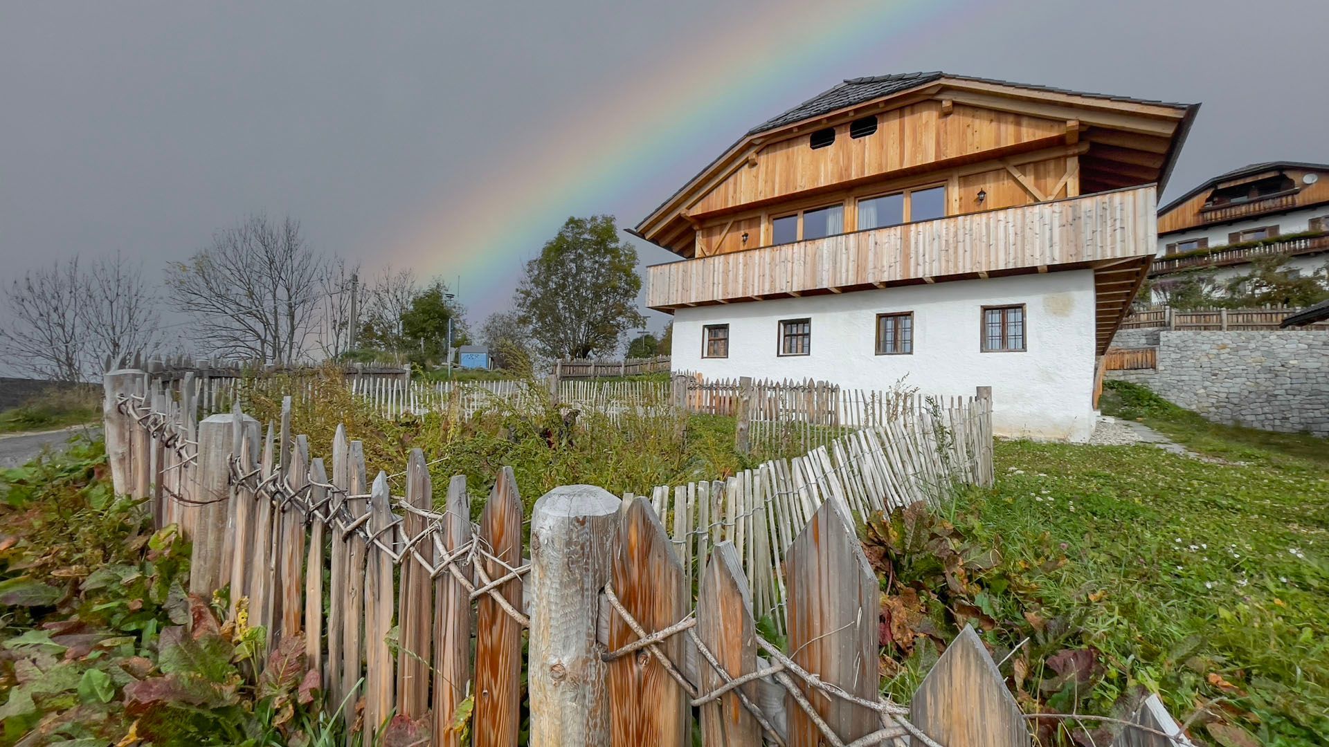 Ein Haus mit einem Holzzaun davor und einem Regenbogen am Himmel.