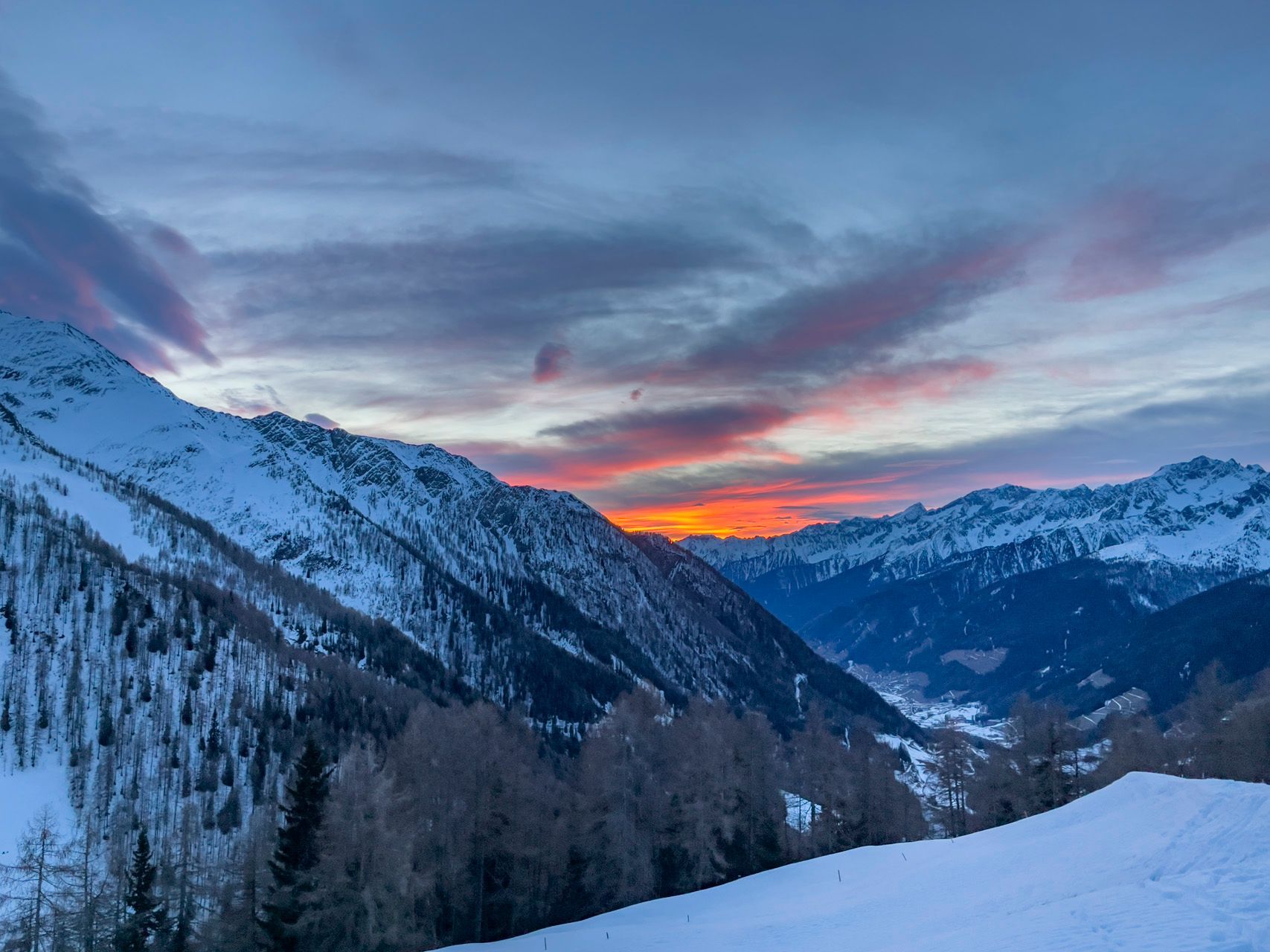 Eine schneebedeckte Bergkette mit einem Sonnenuntergang im Hintergrund