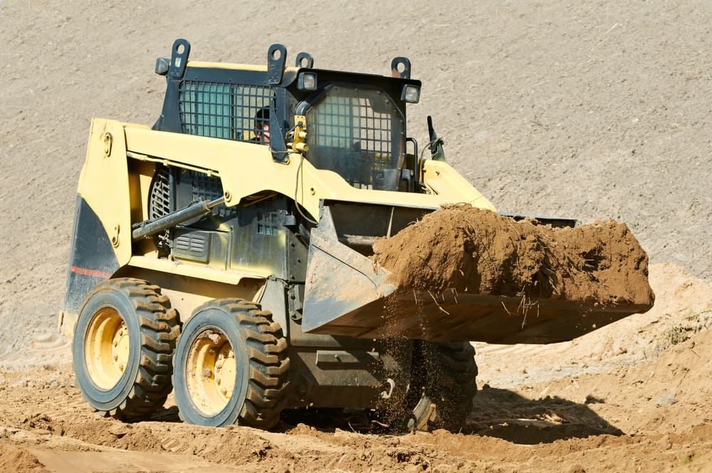 Yellow Skid Steer Loading Dirt at a Construction Site — Machinery & Equipment Hire in Trinity Beach, QLD