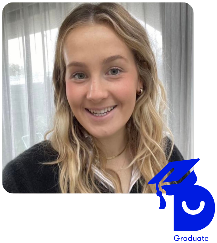 Close up photo of Mia smiling to camera. She has blonde hair and stands in front of a window with sheer curtains.