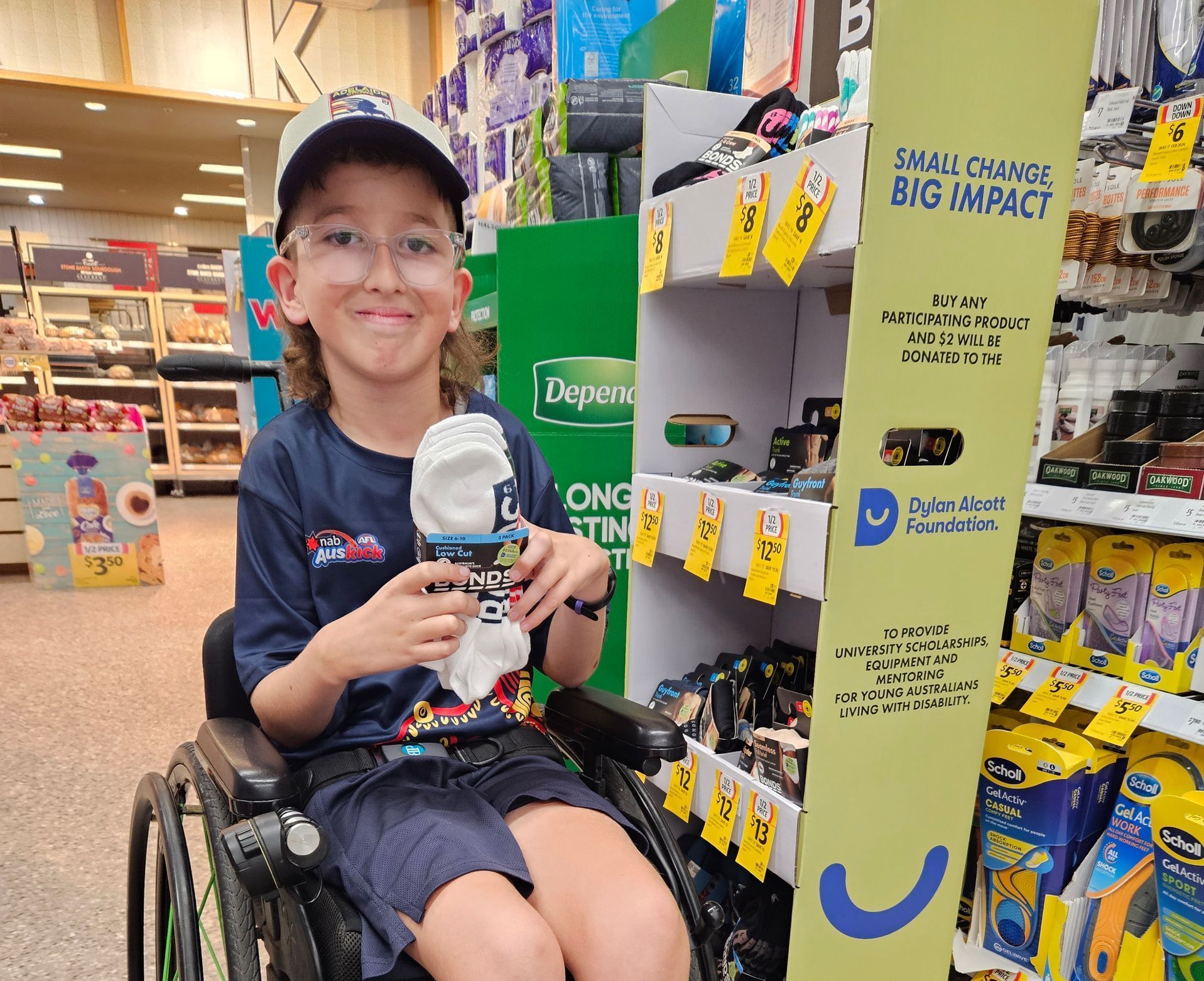 Recipient Alexander is a wheelchair user. He smiles to camera in aisle at a Coles store holding Bond