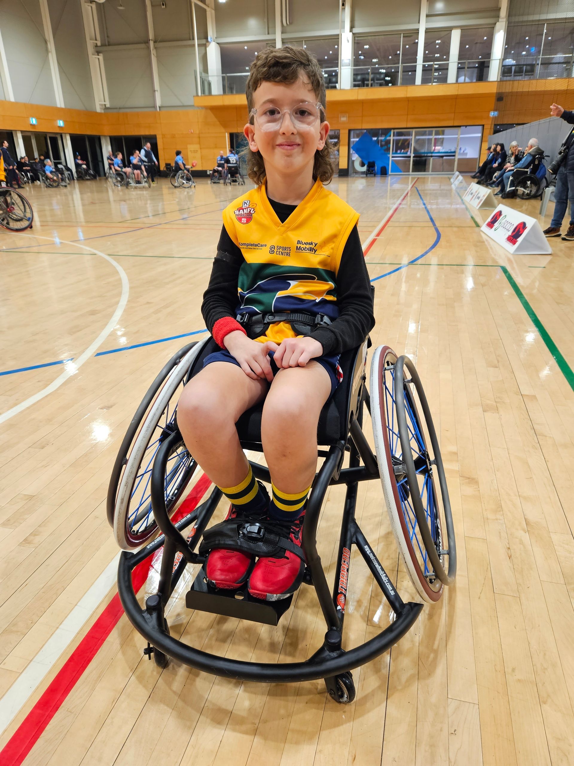 A young boy is sitting in a wheelchair on a basketball court.