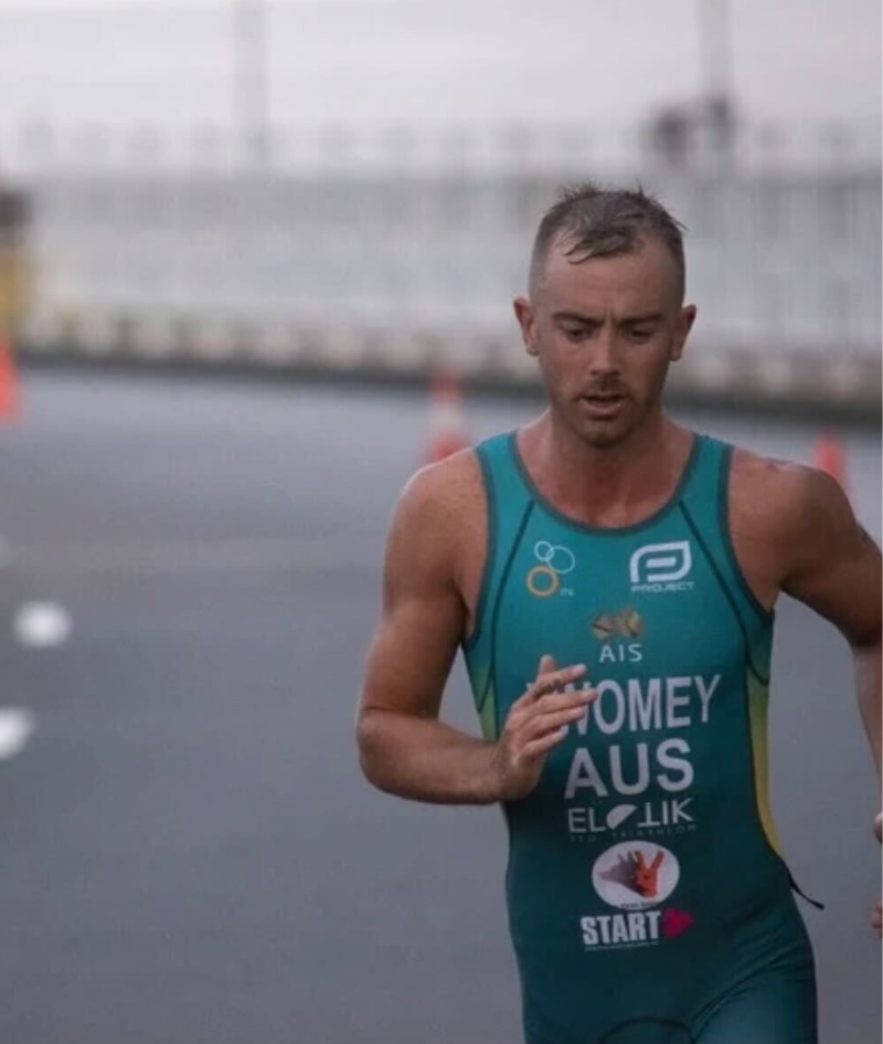 Close up shot of Liam competing in the run leg of a triathlon race. He is mid stride and wearing an Australian tri-suit wth his name and brand logos on the front. 