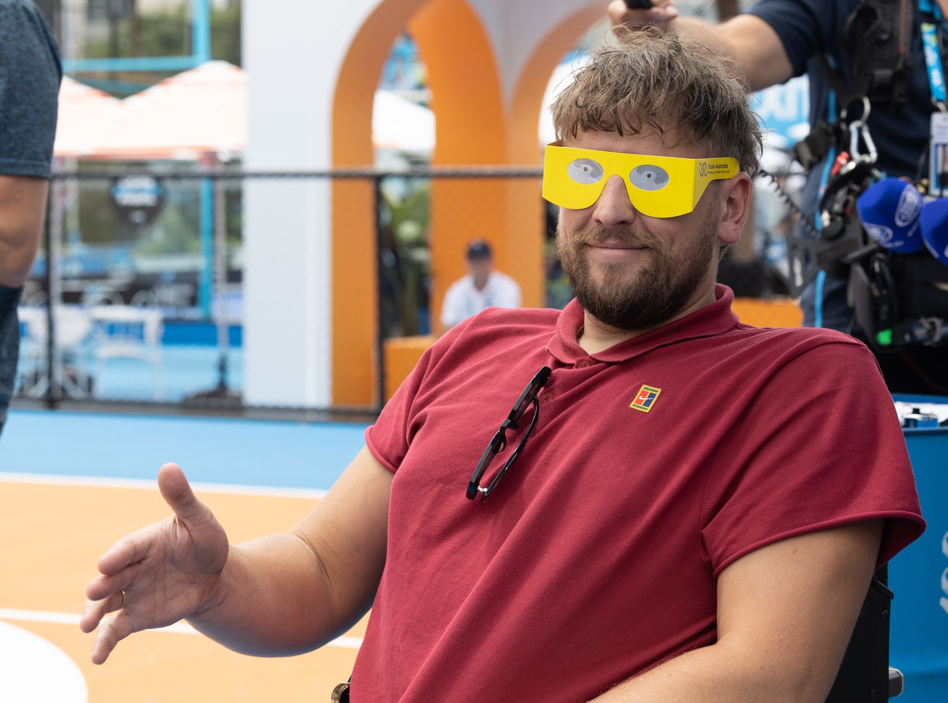 Close up shot of Dylan with an outstretched hand for a hand shake as he wears black out yellow glasses with eyes on the outside.