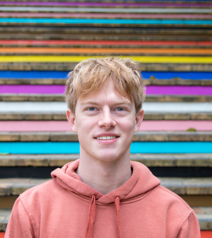 Shot from behind of recipient Jin (right) and Dylan (left) holding hands raised on stage at Ability Fest. Both are wheelchair users.